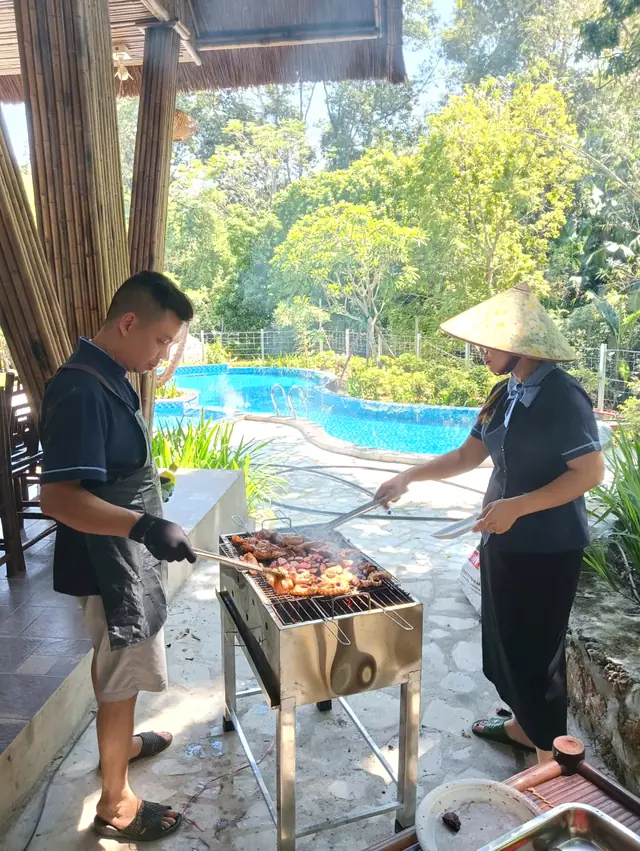 Hai nhân viên nướng thịt trên bếp than cạnh bể bơi giữa vườn cây xanh, Sơn Thủy Retreat