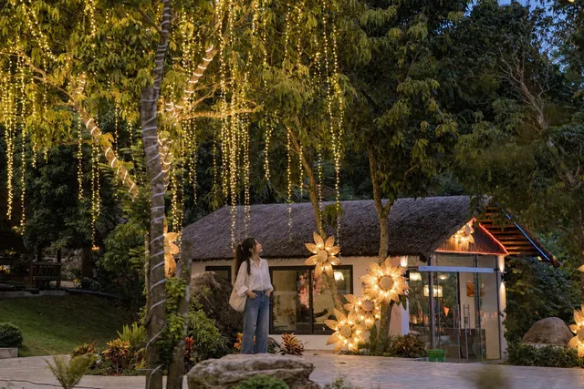 Ảnh minh họa: cô gái đứng dưới dây đèn trước nhà mái tranh ở Sơn Thủy Retreat