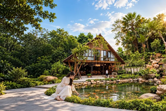 Ảnh minh họa: cô gái ngồi bên hồ cá koi, nhà sàn gỗ phía sau