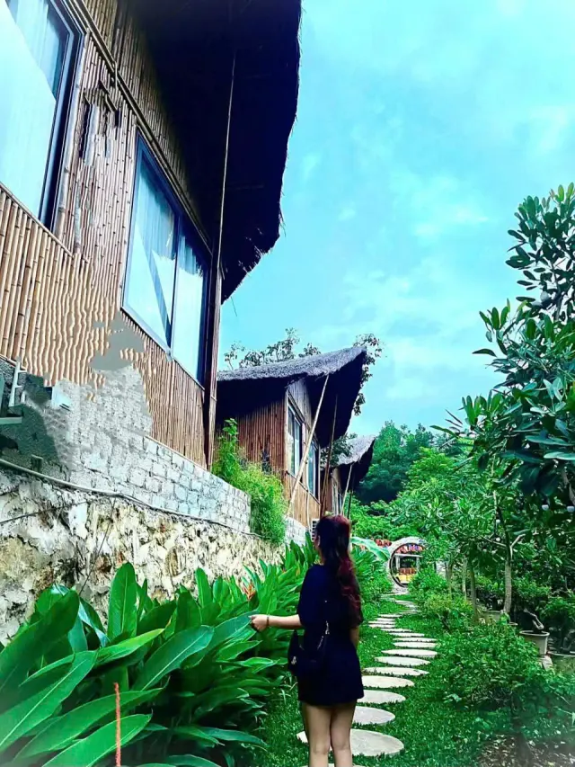 Một chị đi trên lối đá giữa cây xanh cạnh dãy bungalow gỗ