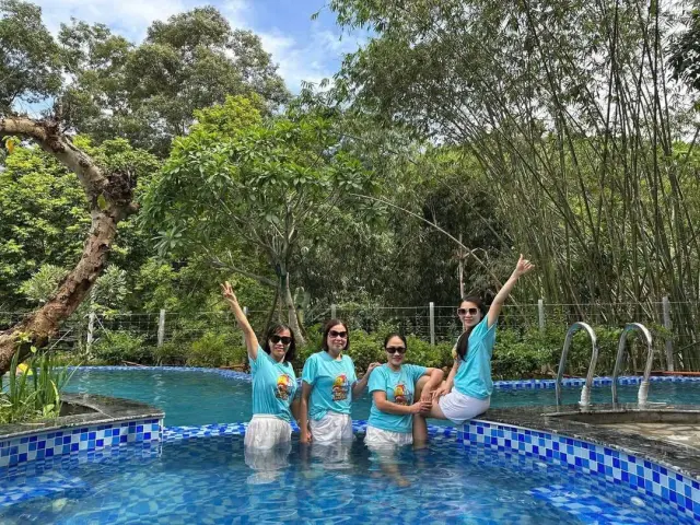 Nhóm bốn chị em mặc áo xanh cùng giơ tay vui vẻ trong bể bơi ngoài trời