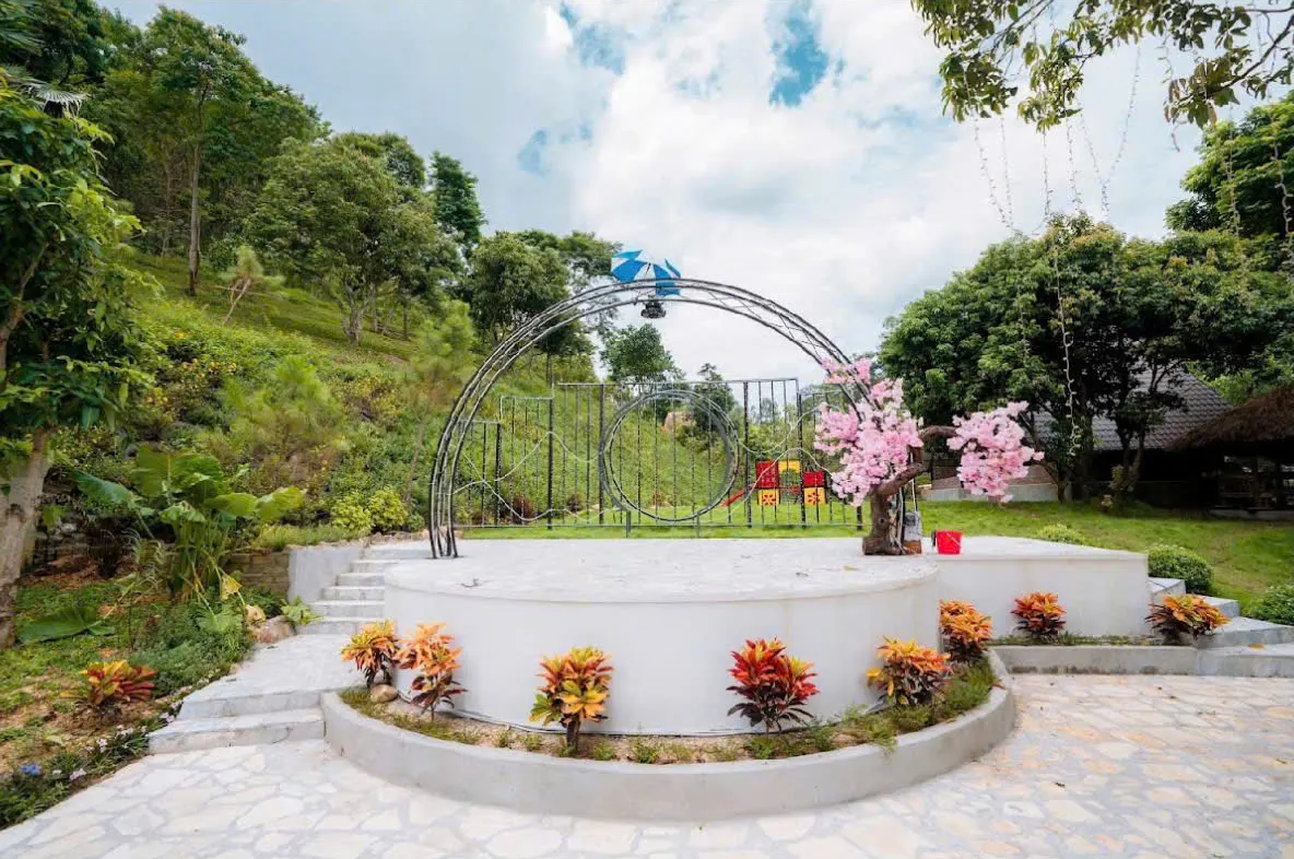 Sân khấu tròn ngoài trời với vòm sắt, cây hoa đào trang trí và bồn hoa lá màu