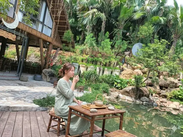 Một chị ngồi pha trà bên bàn gỗ cạnh hồ cá koi