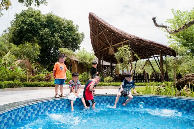 Mấy bé ngồi mép bể bơi ngoài trời, đạp nước dưới nắng
