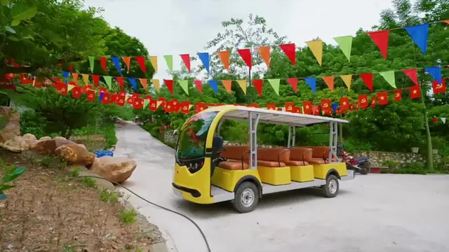 Xe điện vàng của khu đỗ trên đường nội bộ, hai bên cờ đỏ và cây xanh